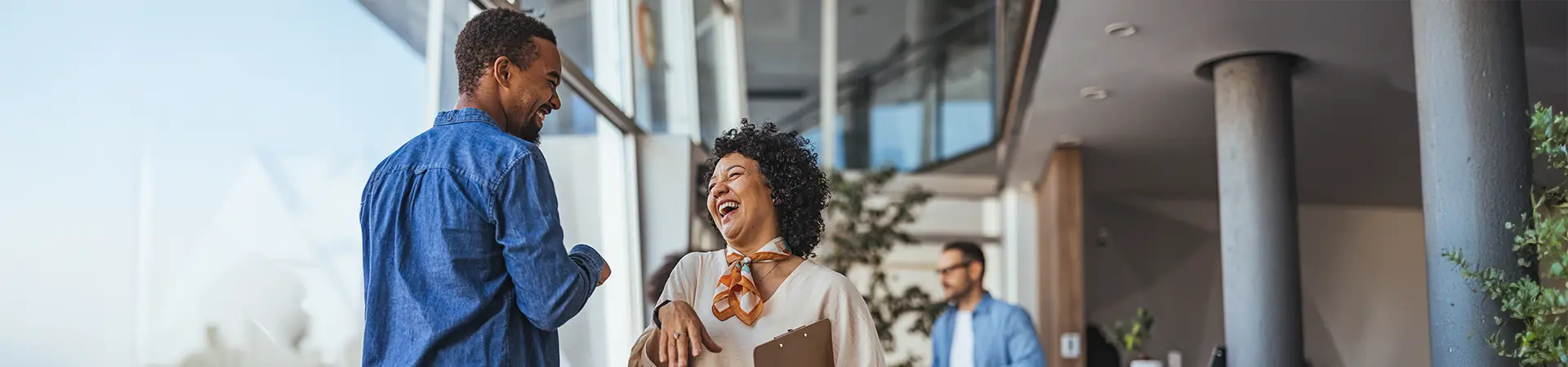 Two colleagues talking and laughing together in a bright office foyer.
