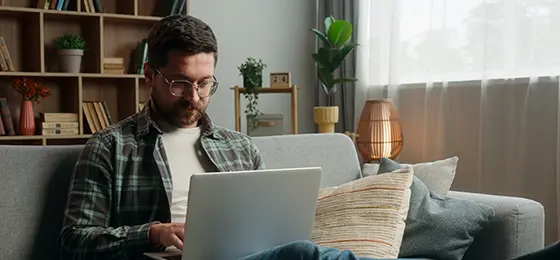 A man working on a laptop while sitting on his sofa at home.