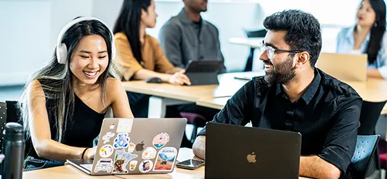 A female and male student working on laptops in a classroom.