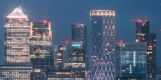An aerial view of multiple tall buildings in the Canary Wharf skyline at night