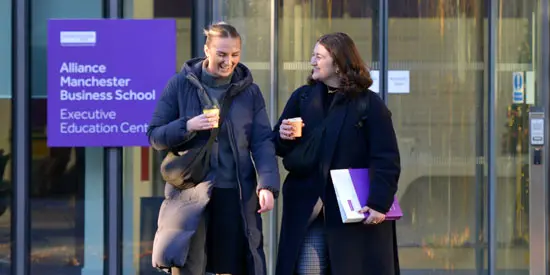 Two students walking in front of the Alliance Manchester Business School Executive Education Centre