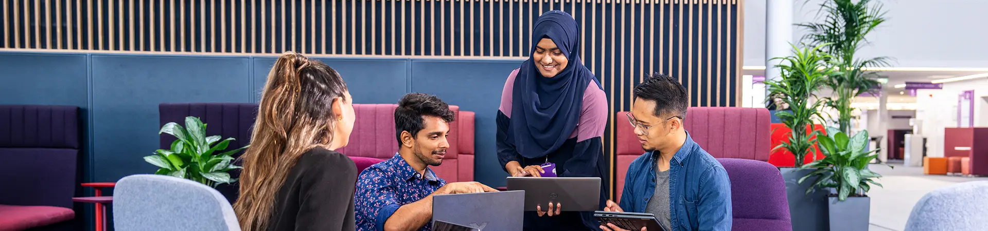 Four students working together on laptops in informal study space at AMBS.