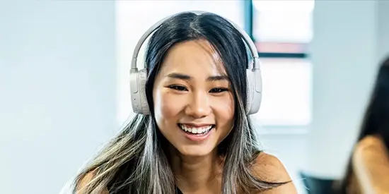Alliance MBS student smiling while studying with headphones in a classroom