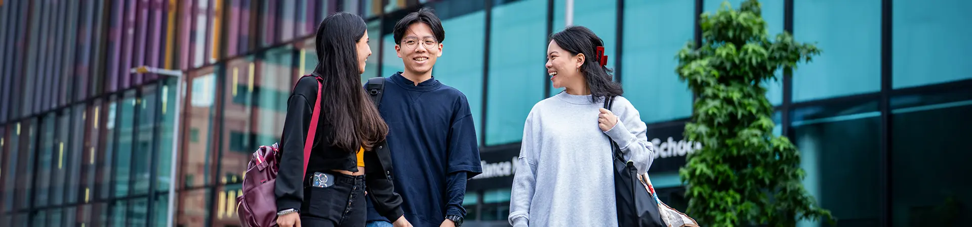 Three masters students walking outside Alliance MBS building.