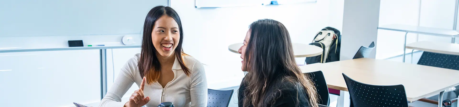 Two female students talking in a classroom.