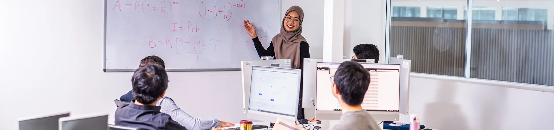 A female student presenting to her classmates in front of a whiteboard.