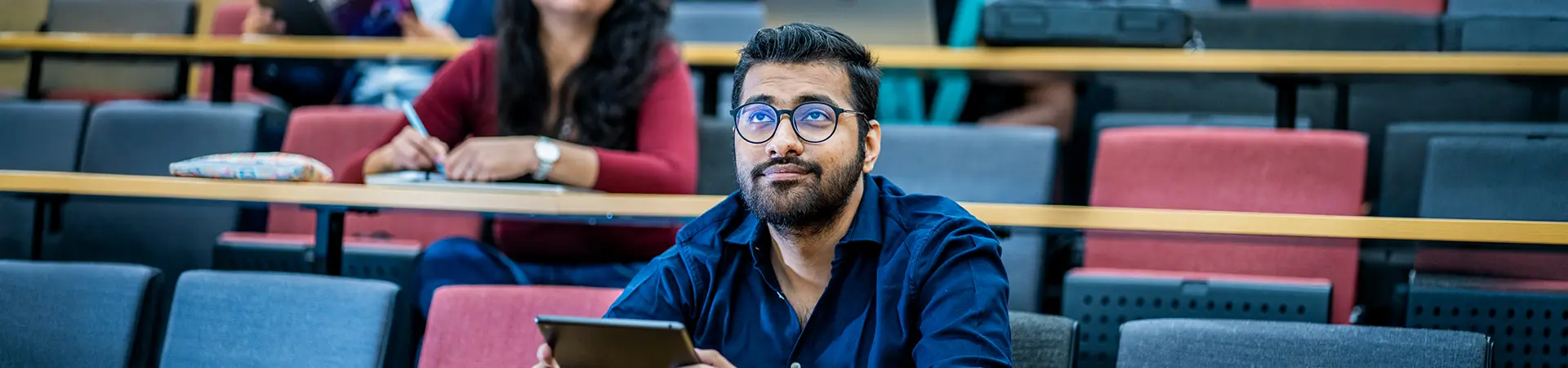 A male student in a lecture theatre holding an ipad.