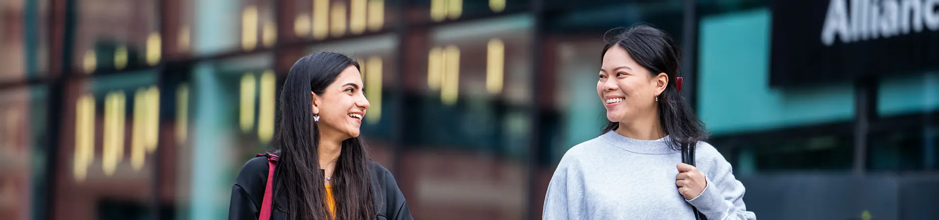 Two female students walking outside AMBS entrance.