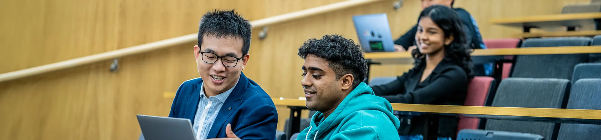 Two male master's students working together on a laptop in a lecture theatre.