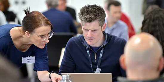 A short course delegate working on a laptop while course leader, Julia Handl explains something beside him.