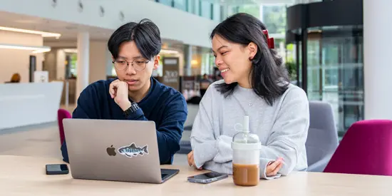 Two students sitting in front of a laptop in the AMBS reception