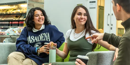 Two students sat facing another student chatting and laughing with coffee