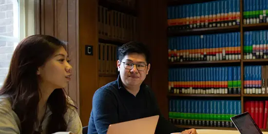 Alliance MBS students studying together in the library with laptops and books