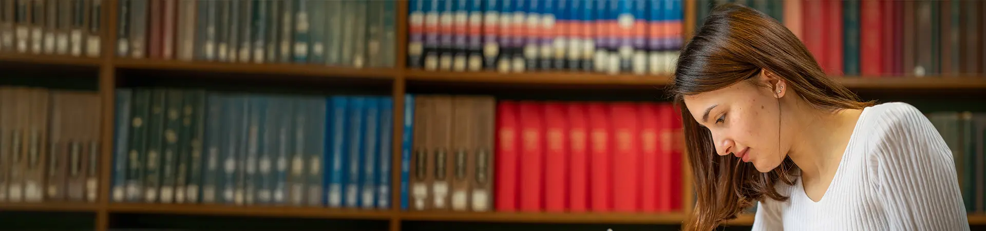A female student sitting in an old university library with books in the background.