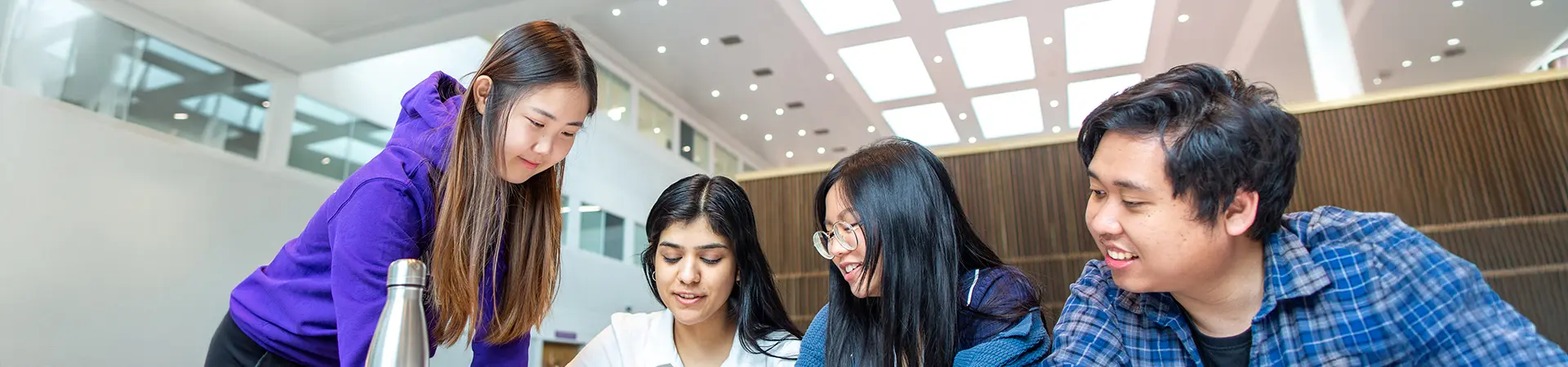 Four students working together on a laptop in an informal study space at AMBS.