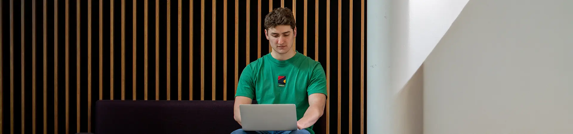 A male student working on a laptop in an informal study space.