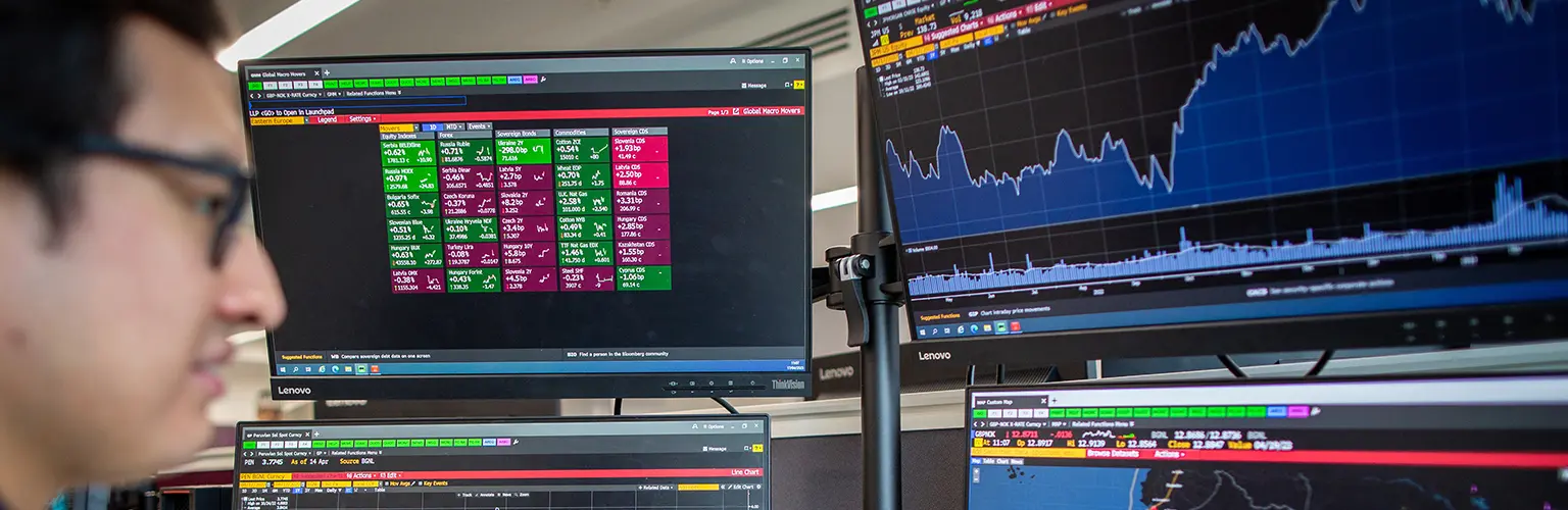 Student working at multiple Bloomberg terminal screens displaying financial data and stock market charts at Alliance MBS.