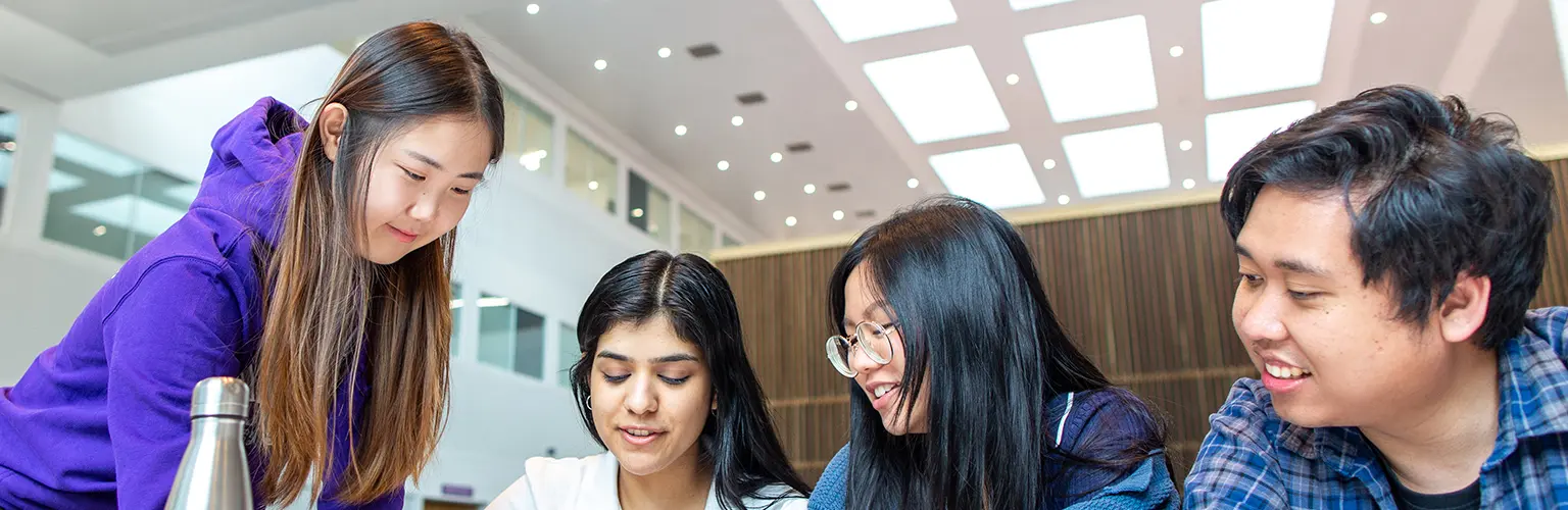 Group of students collaborating on coursework inside Alliance MBS, smiling and working together at a table.