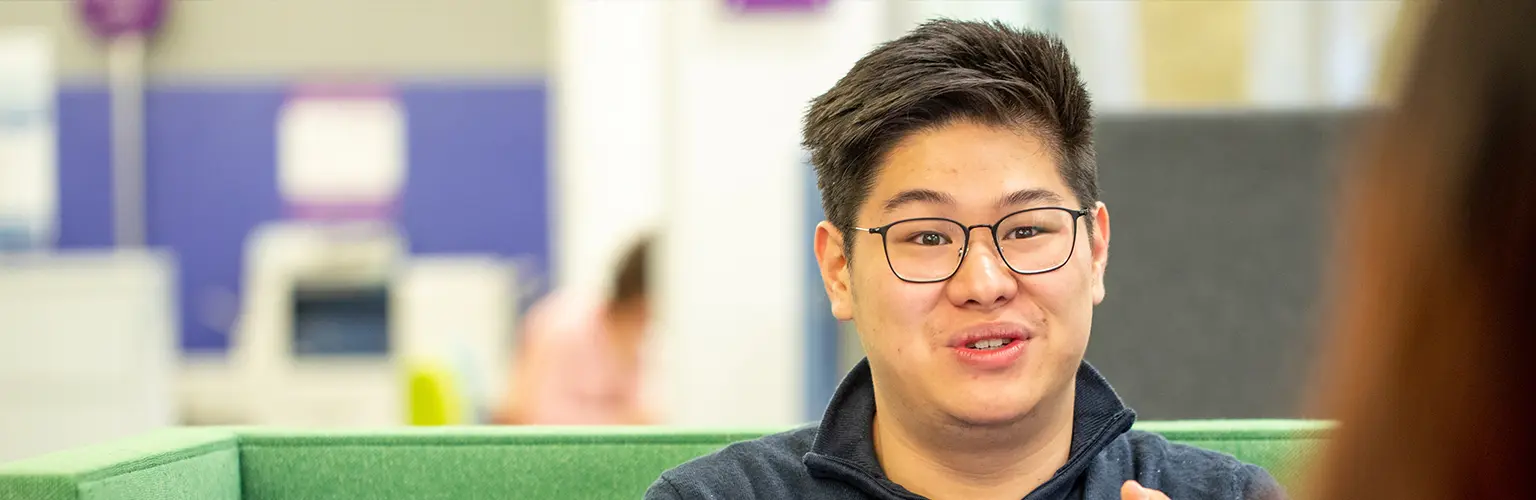 Student wearing glasses speaking during a conversation in a bright, modern study space.