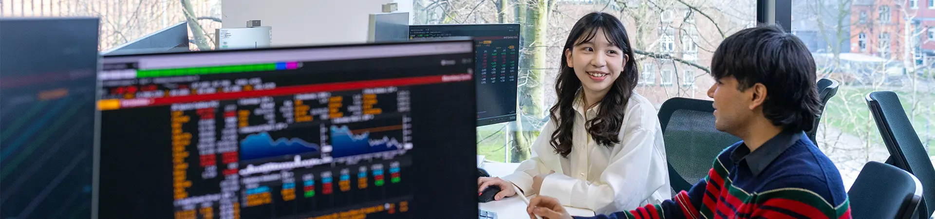 Female and male student working together in computer cluster with screens showing graphs and dashboards.