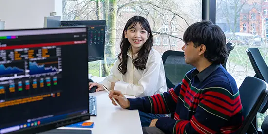Female and male student working together in computer cluster with screens showing graphs and dashboards.