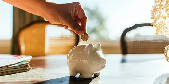 A woman putting a coin in a white piggy bank.
