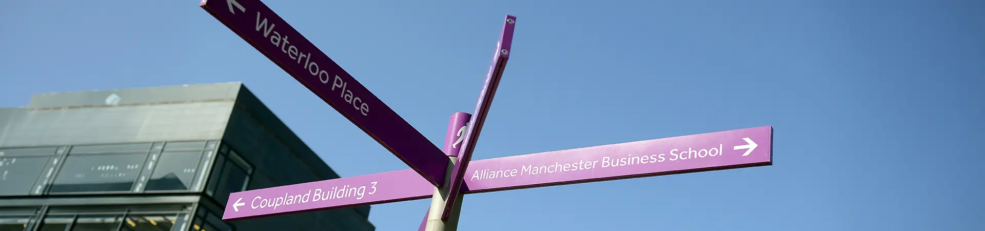 A signpost pointing to Alliance Manchester Business School against a clear blue sky.