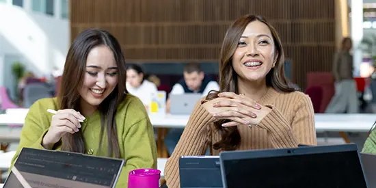 Two female students working on laptops in an informal study area.