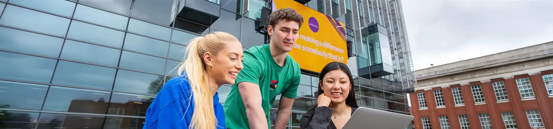 Three undergraduate students working together on a laptop in University of Manchester courtyard.