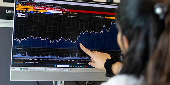 Person pointing at a computer screen showing an upwards trend graph.